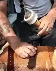 Close-up of hands working a strip of leather with a hand tool